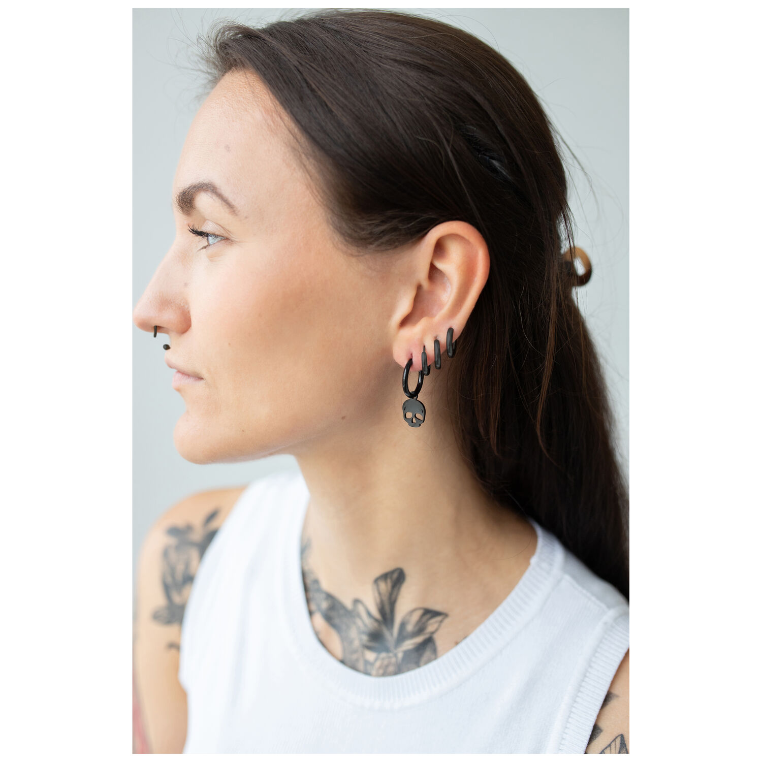 Femme avec des boucles d'oreilles Little Skull Hoops noires en acier chirurgical