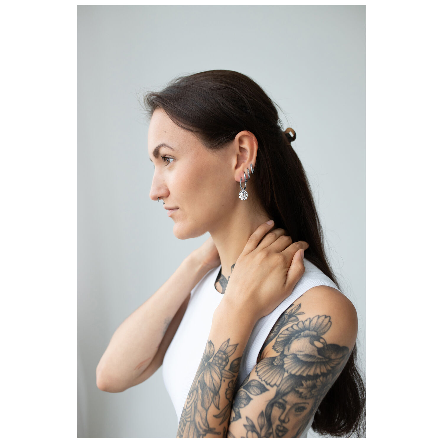 Boucles d'oreilles mandala noires et argentées sur femme Femme aux bras tatoués portant des boucles d'oreilles mandala noires et argentées