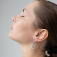 Boucles d'oreilles serpent argentées à l'oreille Profil d'une personne aux yeux fermés portant des boucles d'oreilles serpent argentées, sur fond gris.
