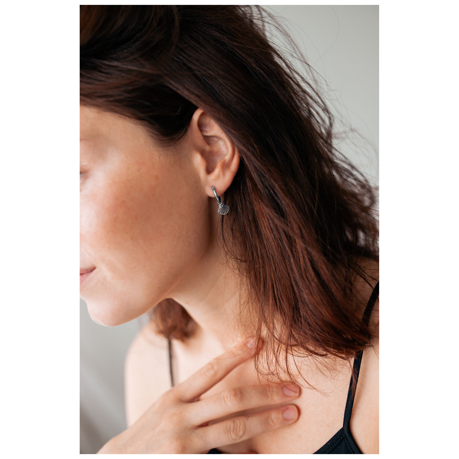 Petites créoles coquillage argentées portées à l'oreille Boucles d'oreilles argentées en forme de coquillage sur une oreille avec des cheveux bruns et une peau claire