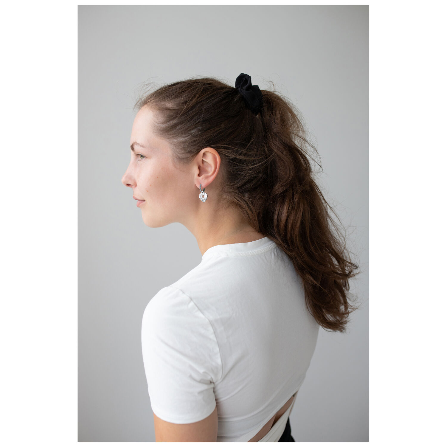 Créoles Cœur Élégantes en Argent Femme en t-shirt blanc portant des créoles cœur en argent sur fond gris