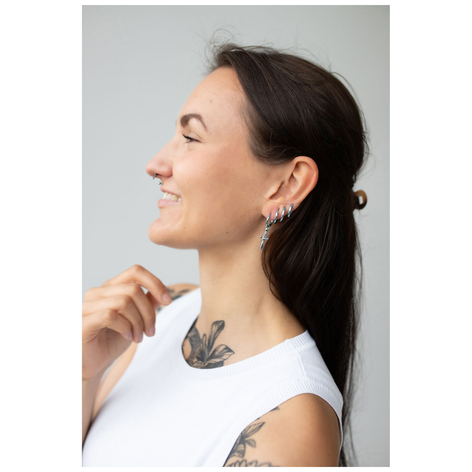 Élégants Boucles d'Oreilles Little Sword Hoops Femme aux longs cheveux foncés portant des boucles d'oreilles Little Sword Hoops argentées sur fond clair
