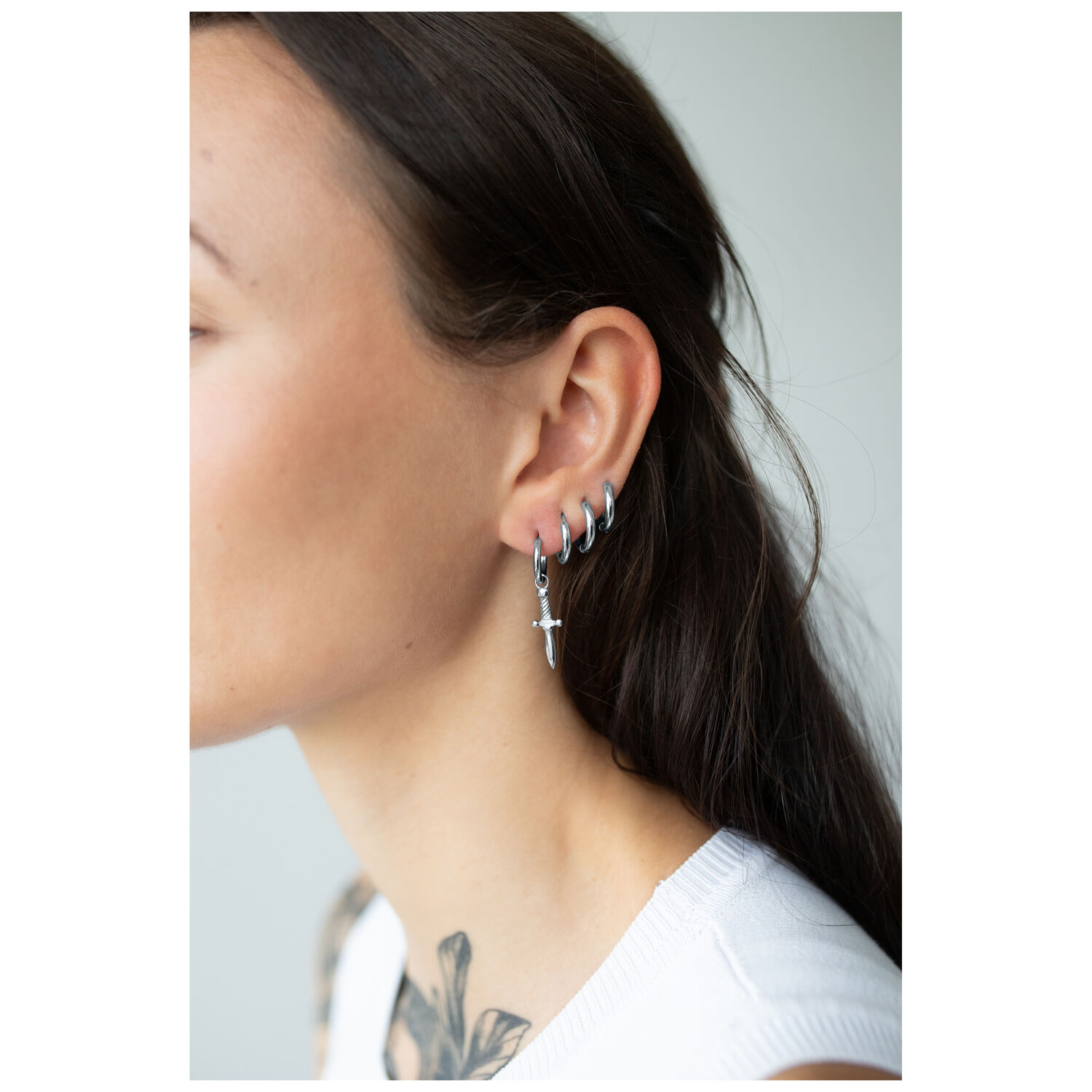 Élégants Little Sword Hoops en argent Boucles d'oreilles en argent en forme d'épée sur une oreille féminine sur fond neutre
