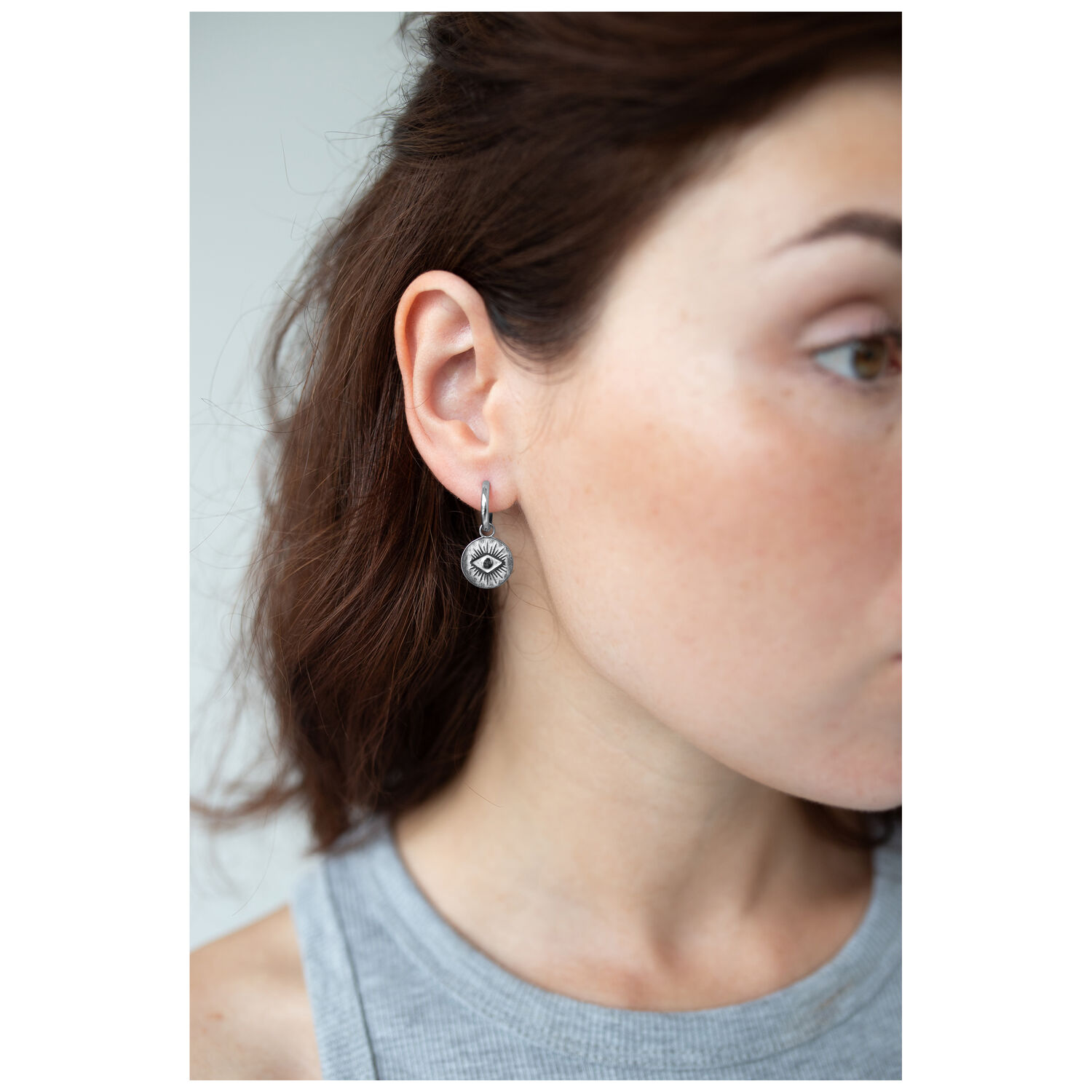 Boucles d'oreilles Little Luminous Eye Hoops argentées Femme portant des boucles d'oreilles argentées avec motif œil, vue de côté