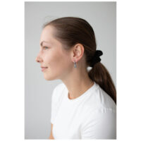 Femme aux cheveux bruns portant des boucles d'oreilles en forme de petits ours noirs, chemise blanche.