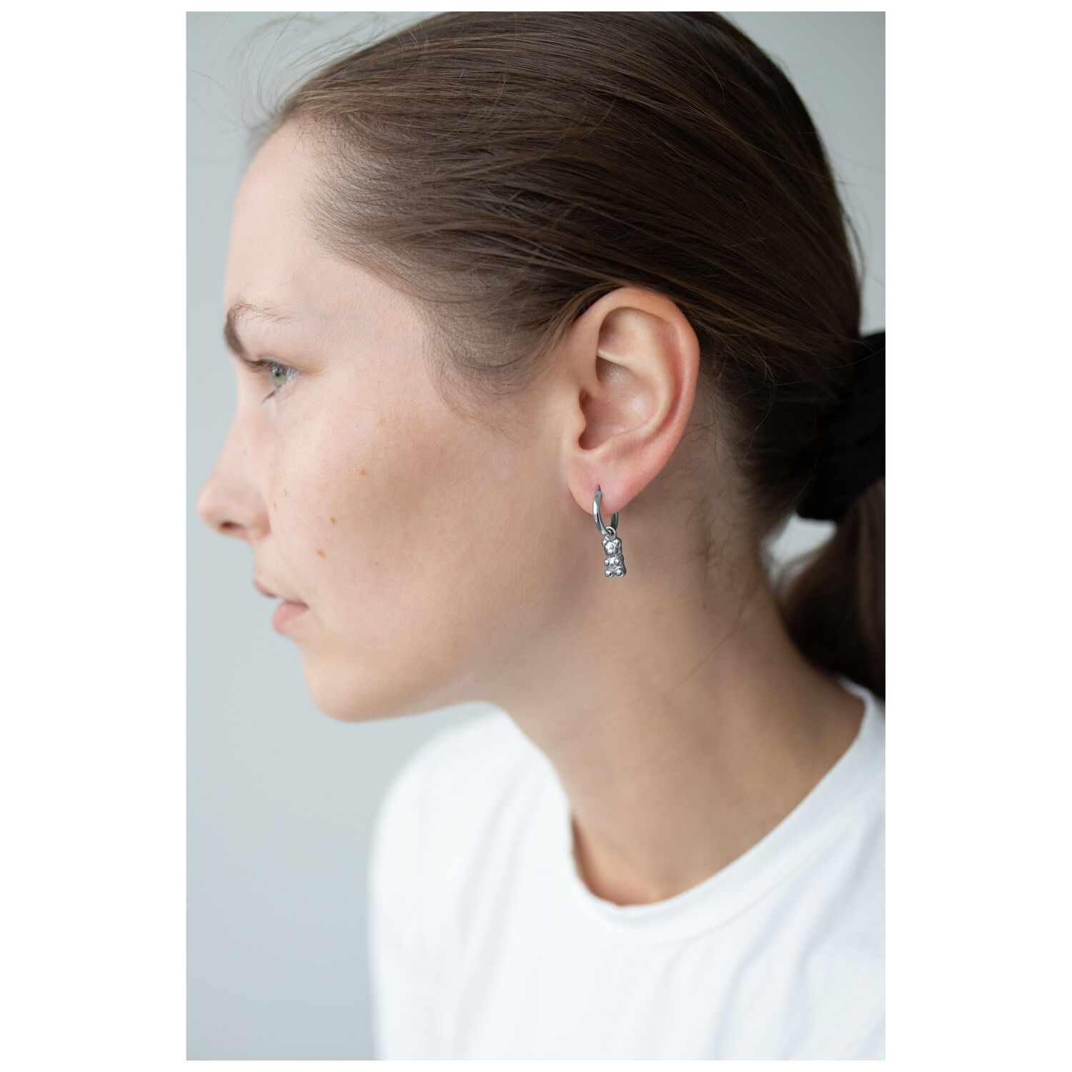 Femme avec des boucles d'oreilles en forme d'oursons en gomme argentés, profil latéral