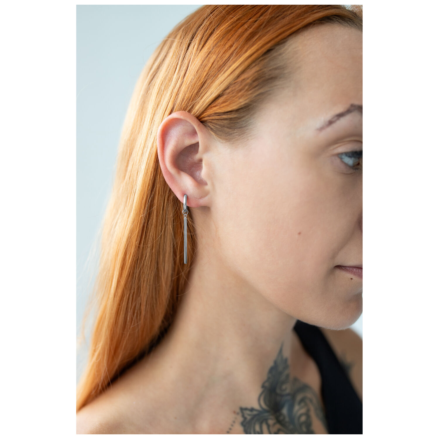 Boucles d'oreilles Bar Hoops élégantes en acier chirurgical Femme aux cheveux longs et lisses portant des boucles d'oreilles Bar Hoops brillantes en acier chirurgical argenté
