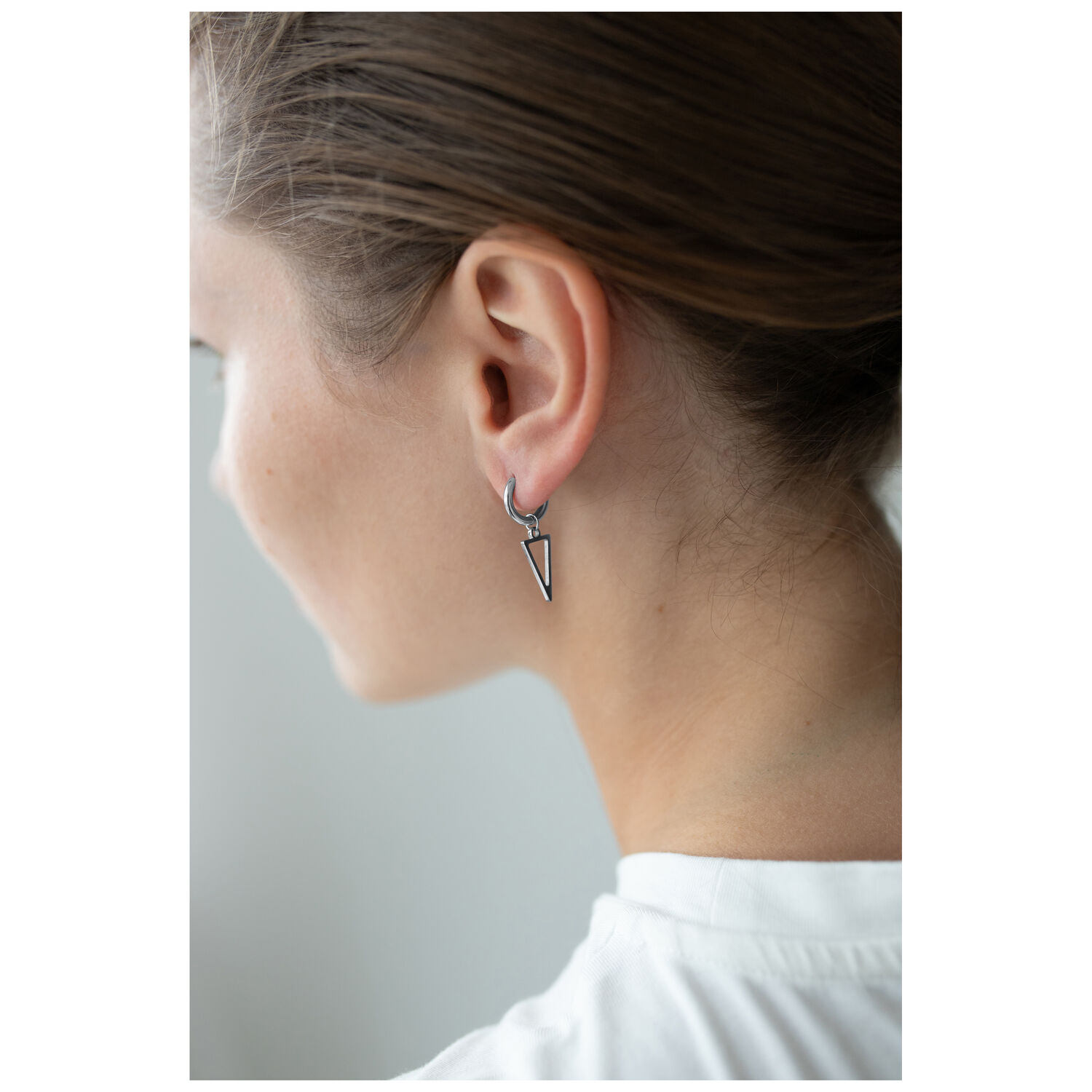Petites créoles triangulaires en noir et argent Créoles triangulaires noires et argentées à l'oreille d'une personne aux cheveux bruns, fond blanc