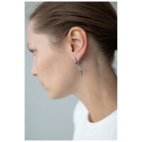 Petites boucles d'oreilles croix en acier chirurgical Femme avec petites boucles d'oreilles croix en acier chirurgical noir et argent devant un fond gris