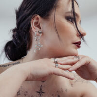 Petites créoles croix en argent à l'oreille d'une femme Femme avec petites créoles croix en argent et boucle d'oreille serpent, fond blanc