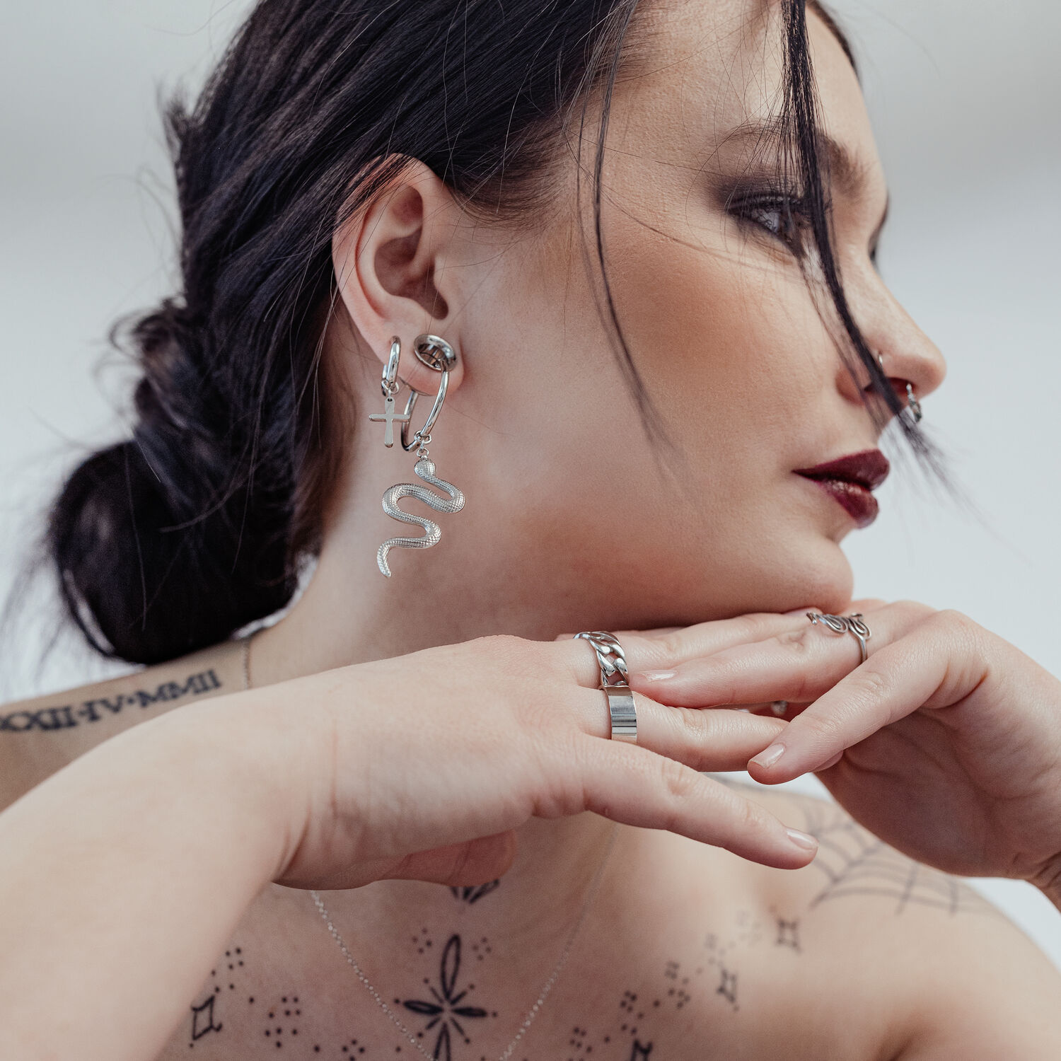 Petites créoles croix en argent à l'oreille d'une femme Femme avec petites créoles croix en argent et boucle d'oreille serpent, fond blanc