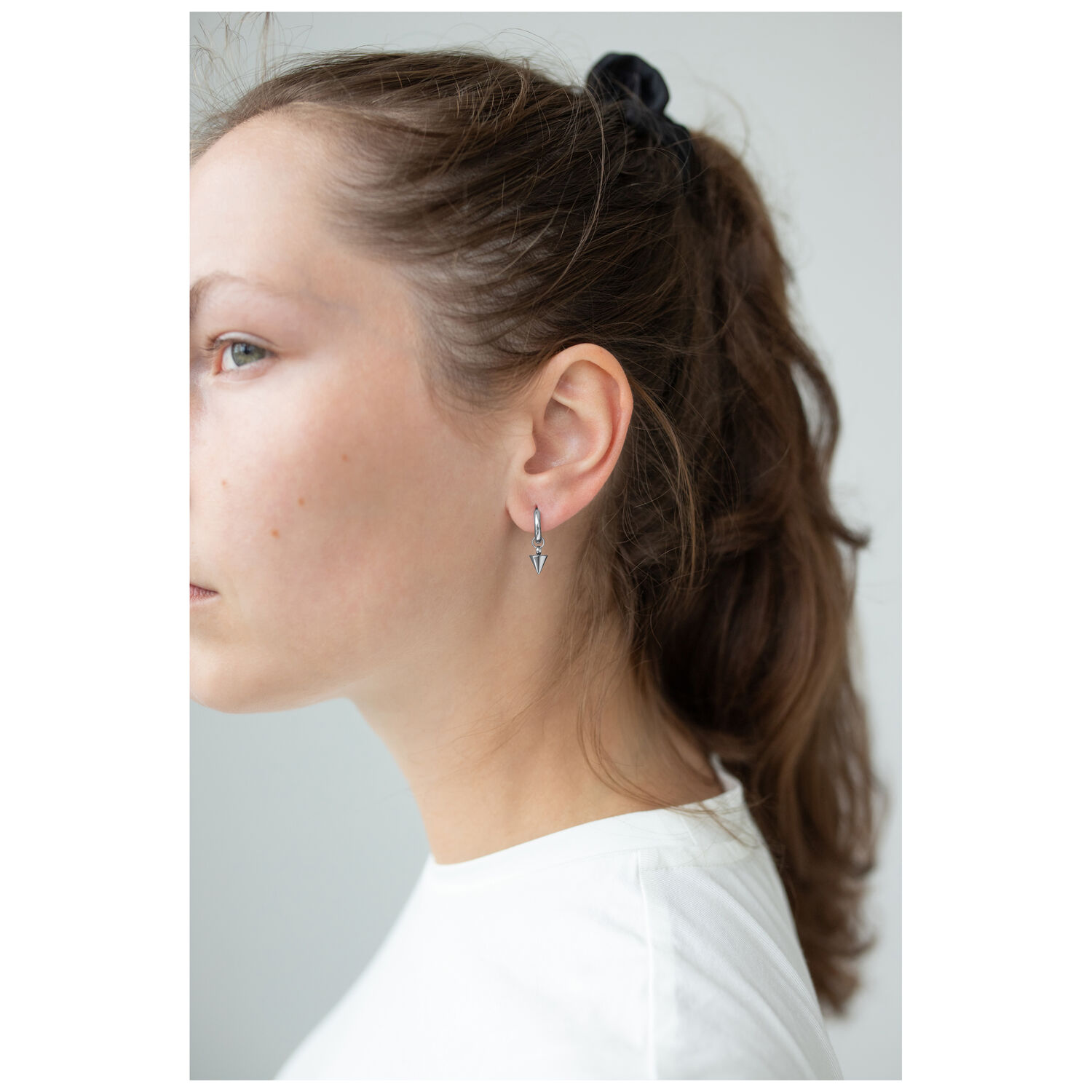 Petites créoles à pointes en acier chirurgical Femme portant de petites créoles noires à pointes à son oreille, fond blanc