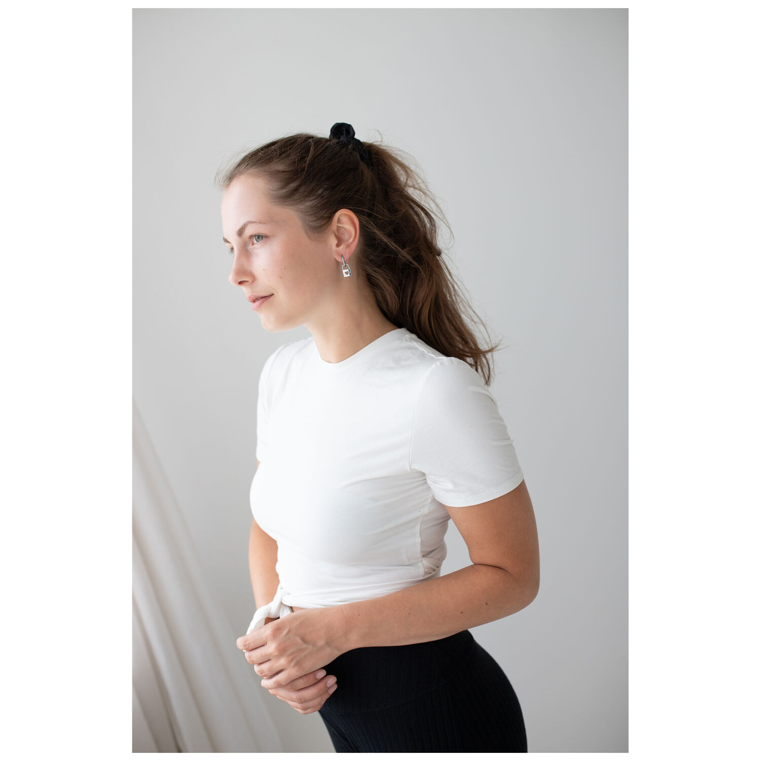 Femme avec t-shirt blanc et élégantes boucles d'oreilles en argent sur fond neutre