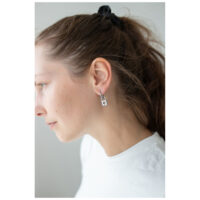 Femme portant des boucles d'oreilles Little Lock Hoops en argent sur fond blanc