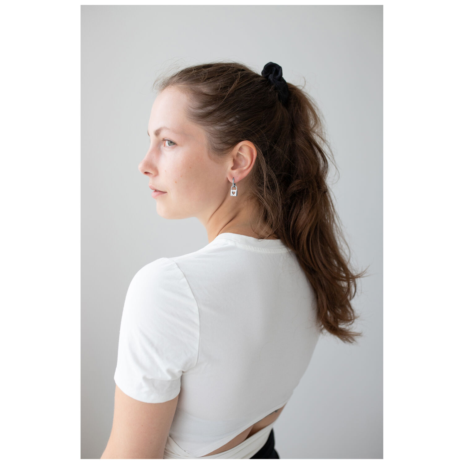 Femme aux cheveux longs portant des boucles d'oreilles Little Lock Hoops en argent sur fond blanc