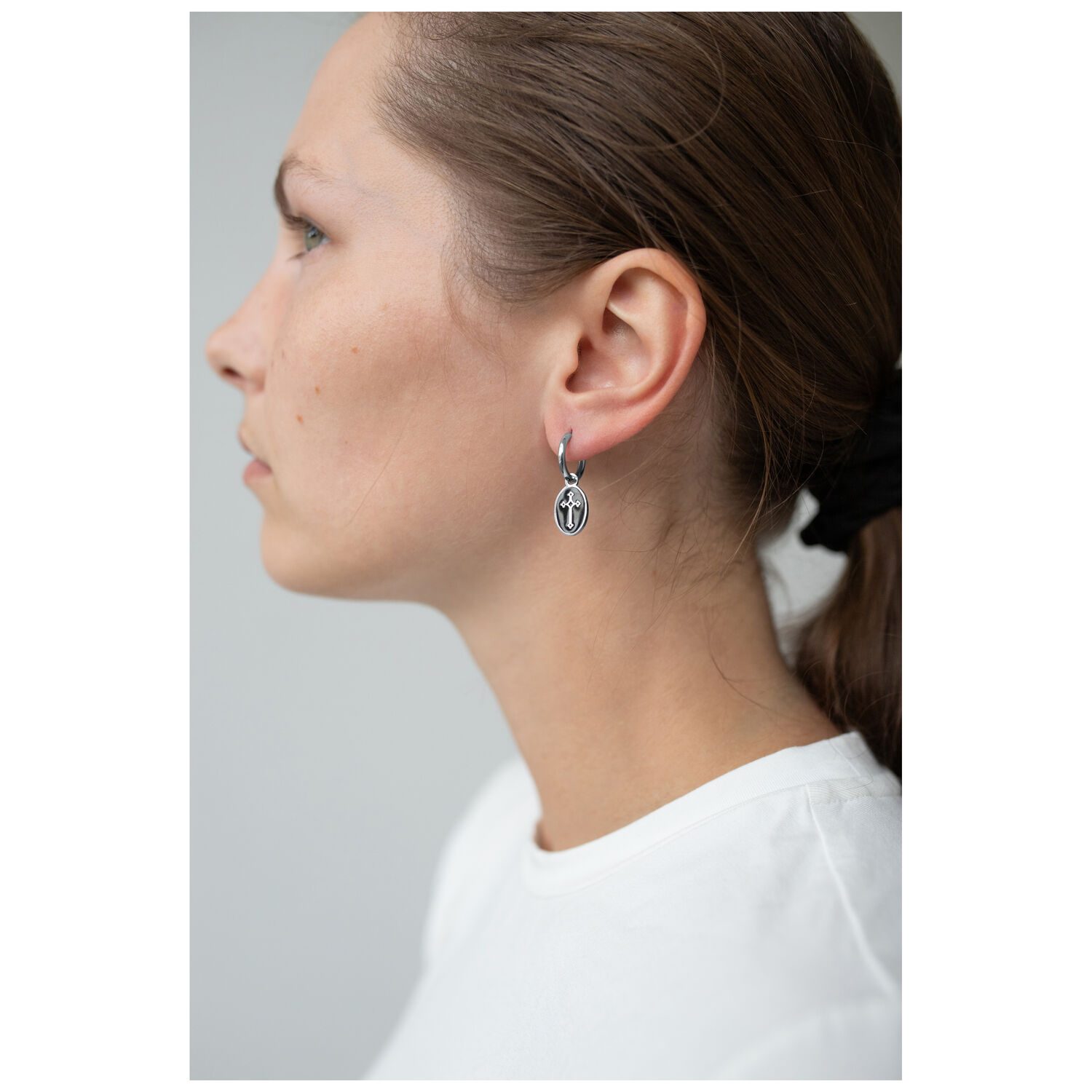 Boucles d'oreilles croix argentées au design vintage Vue latérale d'une femme avec des boucles d'oreilles croix argentées sur fond clair