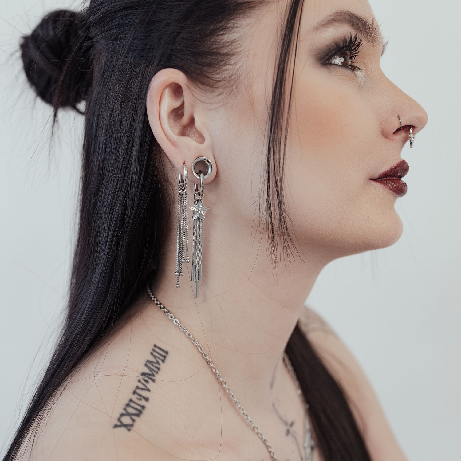 Petites créoles étoile filante argentées à l'oreille Femme aux longs cheveux noirs portant des petites créoles étoile filante argentées et ayant des tatouages sur le cou.