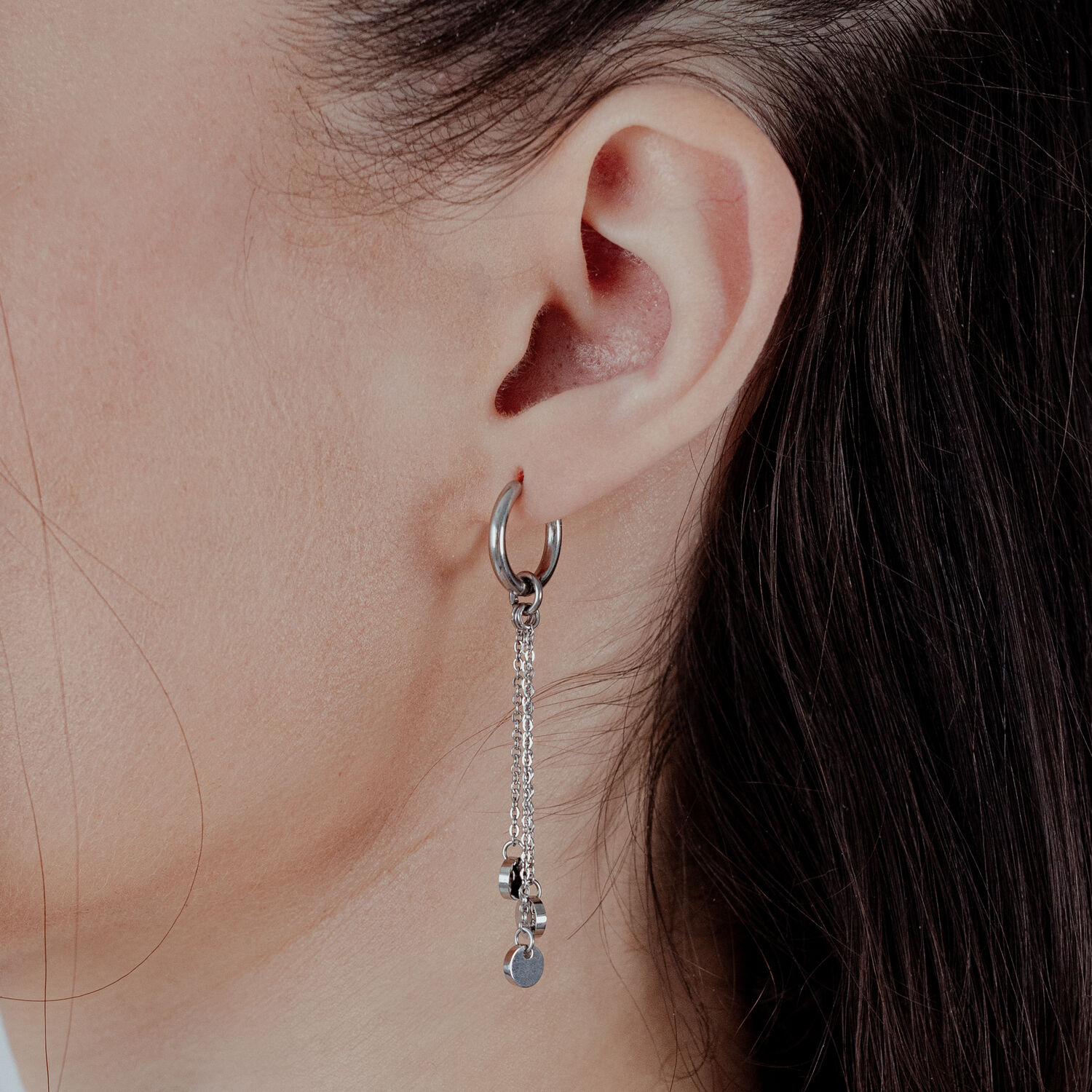 Petites créoles en acier inoxydable avec pendentif chaîne Créoles argentées avec pendentif chaîne à une oreille féminine sur fond clair