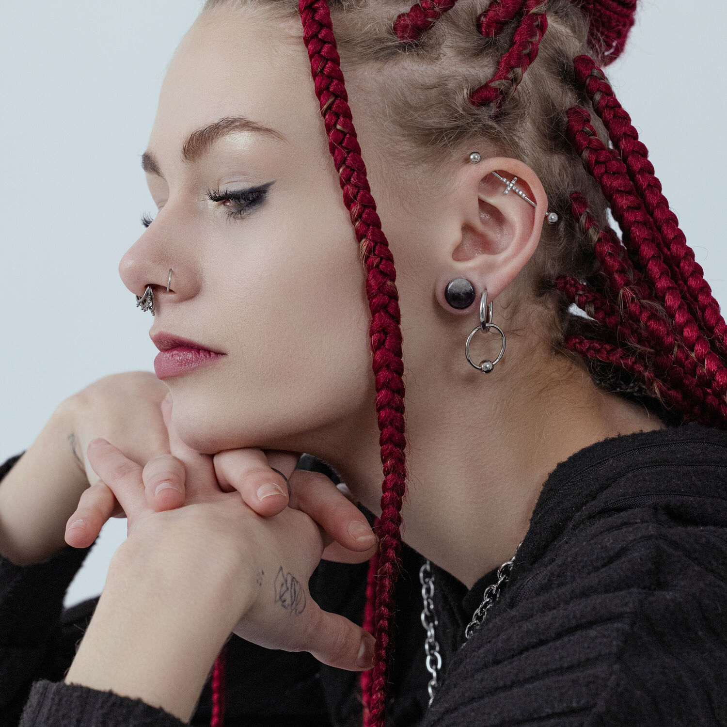 Petites créoles à fermoir boule argentées portées à l'oreille Femme aux dreadlocks rouges portant des boucles d'oreilles argentées et des piercings au nez, profil latéral