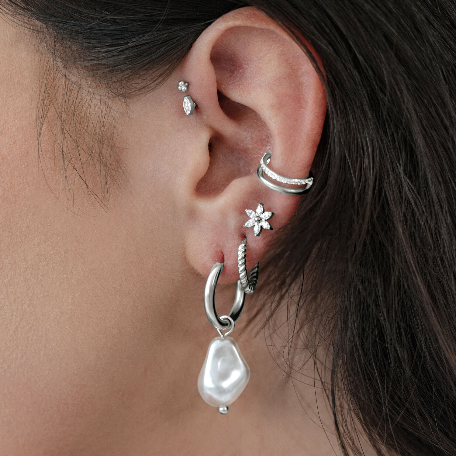 Boucles d'oreilles en perles baroques argentées sur une oreille avec plusieurs piercings.