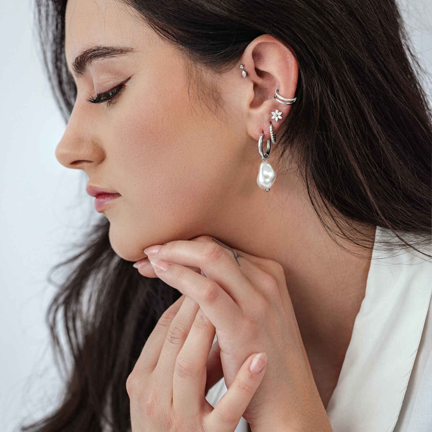 Vue de côté d'une femme avec des créoles en perles baroques et d'autres boucles d'oreilles sur fond clair