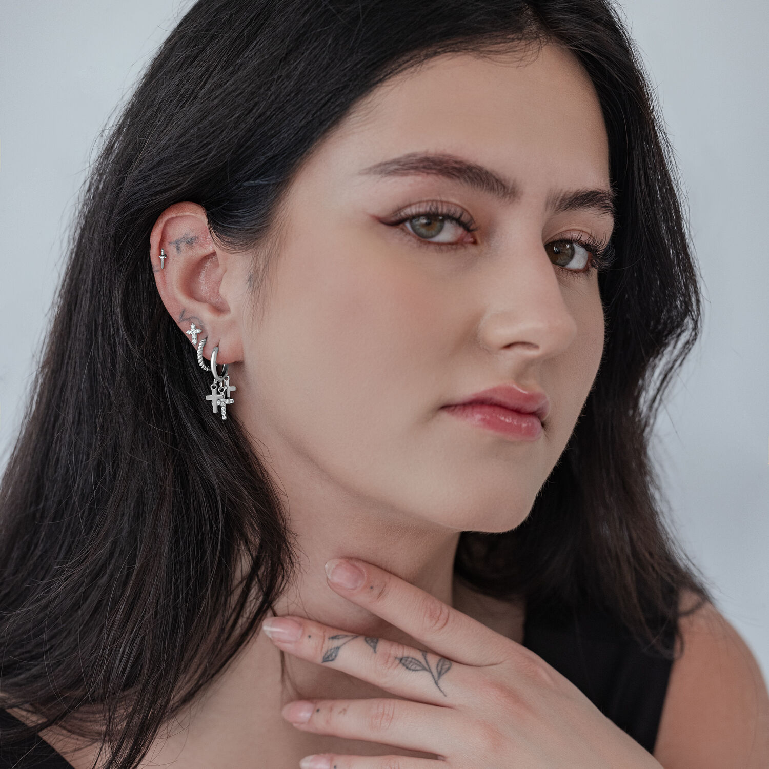 Créoles avec petits pendentifs croix en acier inoxydable Femme aux cheveux noirs portant des créoles en croix argentées sur fond blanc