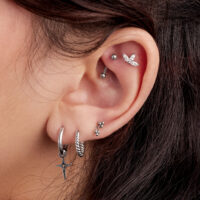 Créoles Mini-Polar Star argentées Gros plan d'une oreille avec plusieurs boucles d'oreilles argentées, y compris une paire de créoles Mini-Polar Star.
