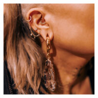 Oreille avec chaîne de piercing dorée et goutte de cristal, vue détaillée