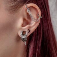 Chaîne de piercing double en argent Oreille avec plusieurs piercings en argent et une chaîne sur fond blanc