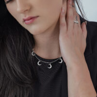 Collier Little Moon argenté avec pendentifs Femme portant un collier Little Moon argenté avec plusieurs pendentifs lune sur un haut noir