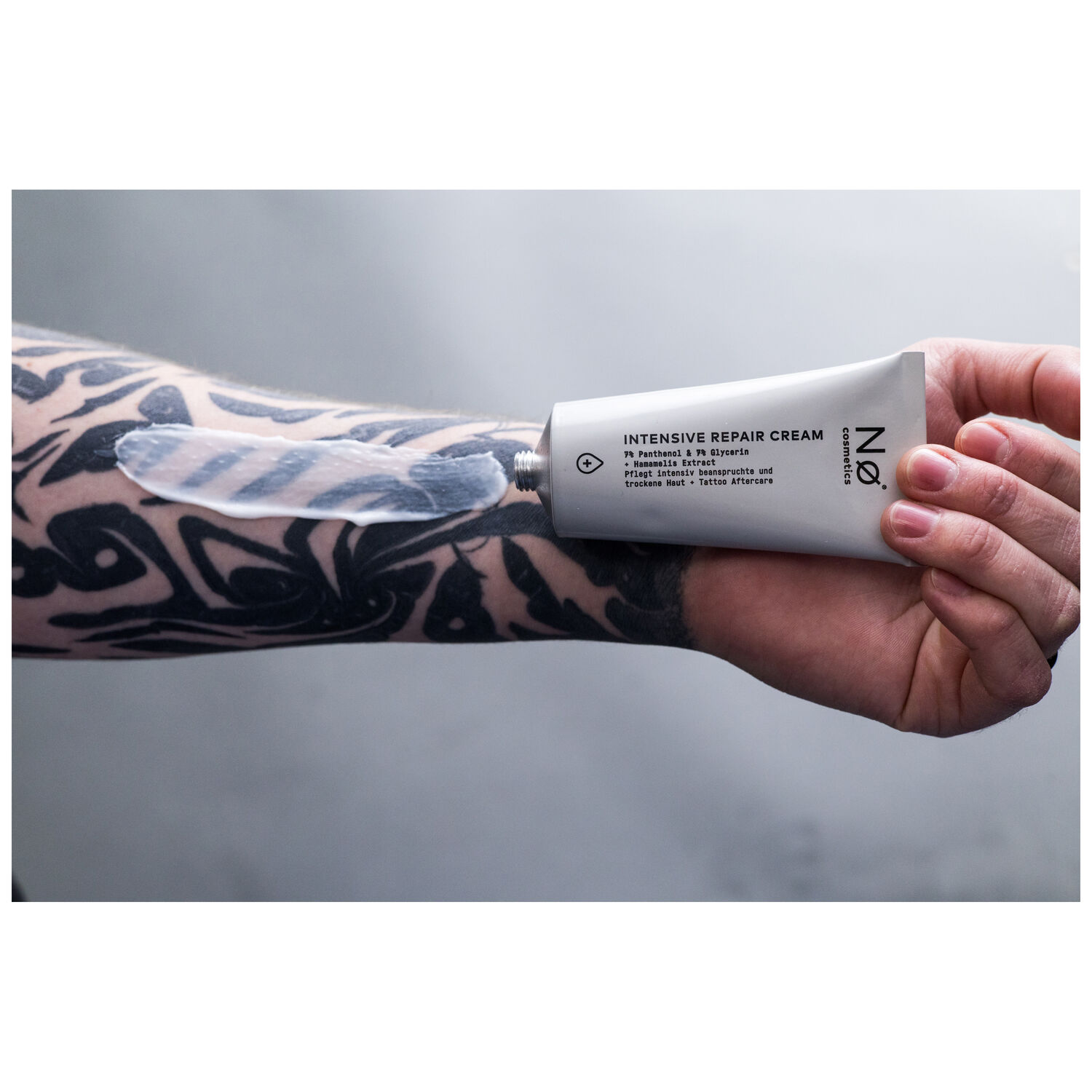 No Cosmetics Crème Réparatrice Intensive 20ml Tube gris-blanc de la Crème Réparatrice Intensive de No Cosmetics, tenue par une main tatouée