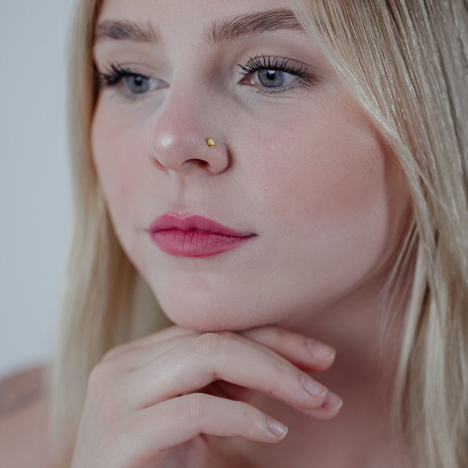 Clou de nez en or 18K cristal clair Clou de nez en or dans le nez d'une femme, cheveux blonds, fond neutre