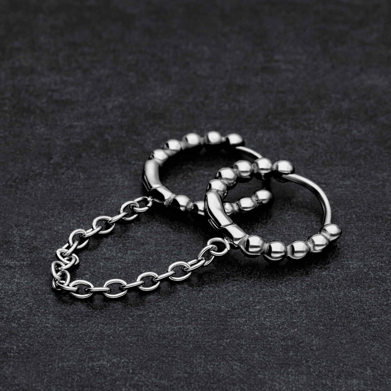 Anneaux Huggie à Double Perle en Acier Chirurgical Deux anneaux Huggie noirs reliés avec des perles sur fond sombre