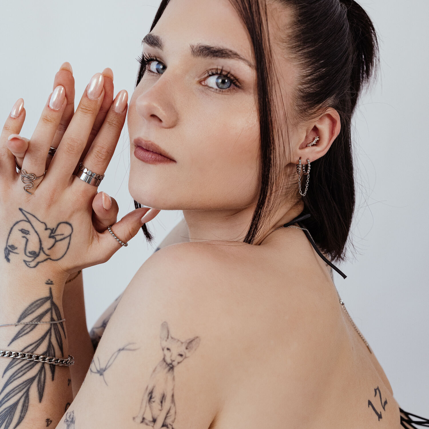 Double Huggie Ball Hoops sur modèle Femme aux bras tatoués portant des anneaux de piercing noirs et argentés à l'oreille, profil latéral