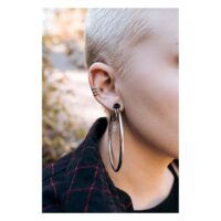 Boucles d'oreilles noires ajourées portées à l'oreille Gros plan d'une oreille avec de grandes boucles d'oreilles noires ajourées de Wildcat