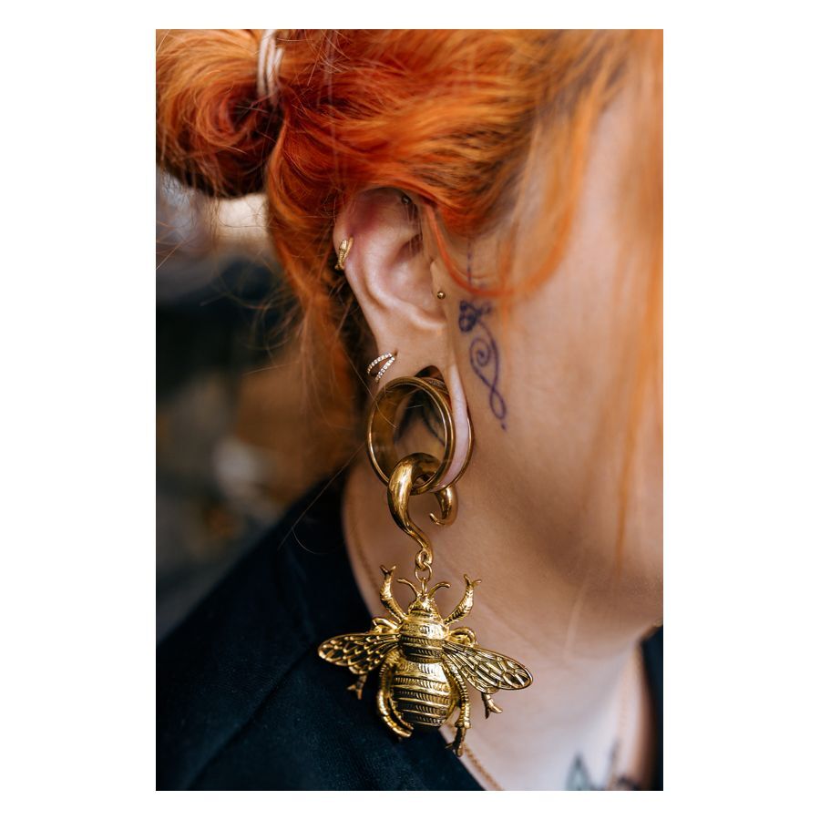 Clicker double cristal doré dans l'oreille Piercing clicker doré dans l'oreille d'une personne aux cheveux rouges et tatouage
