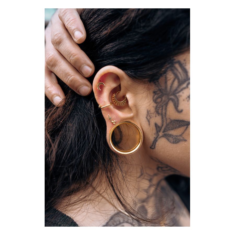 Barbell d'oreille Luna doré porté dans l'oreille Barbell d'oreille Luna doré dans l'oreille d'une personne tatouée aux cheveux noirs