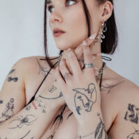 Personne avec anneau serpent et tatouages, portant des bijoux sur fond blanc