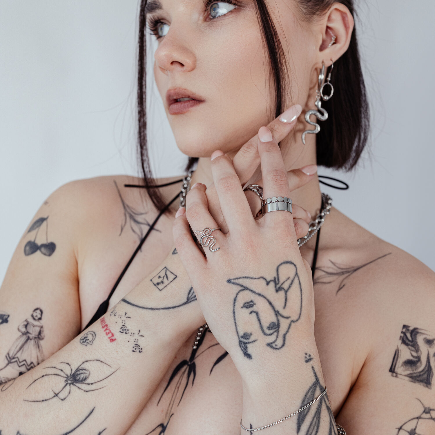 Personne avec anneau serpent et tatouages, portant des bijoux sur fond blanc