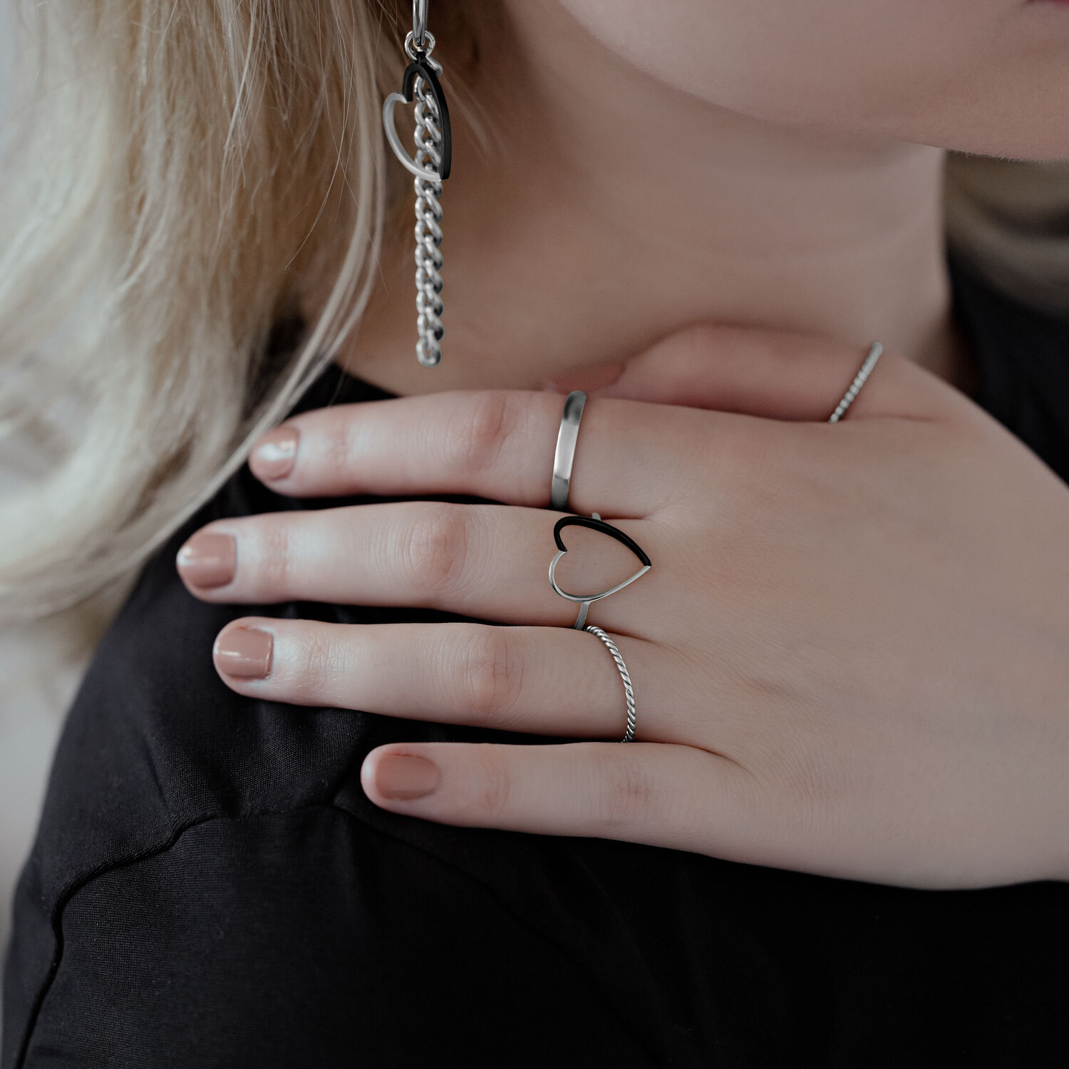 Bague cœur bicolore en acier chirurgical Gros plan d'une main portant une bague cœur bicolore en acier chirurgical, aux côtés d'autres bagues