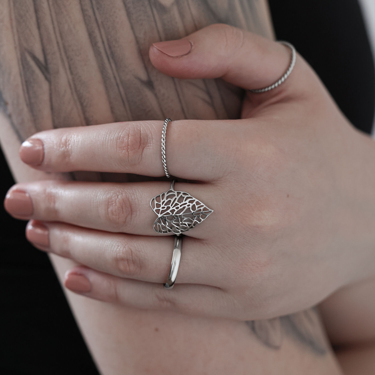 Anneau Lovely Leaf argenté sur la main Anneau feuille argenté en acier chirurgical sur une main tatouée devant un fond clair
