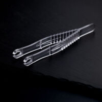 Deux pinces à piercing rondes et stériles transparentes croisées sur un fond sombre.