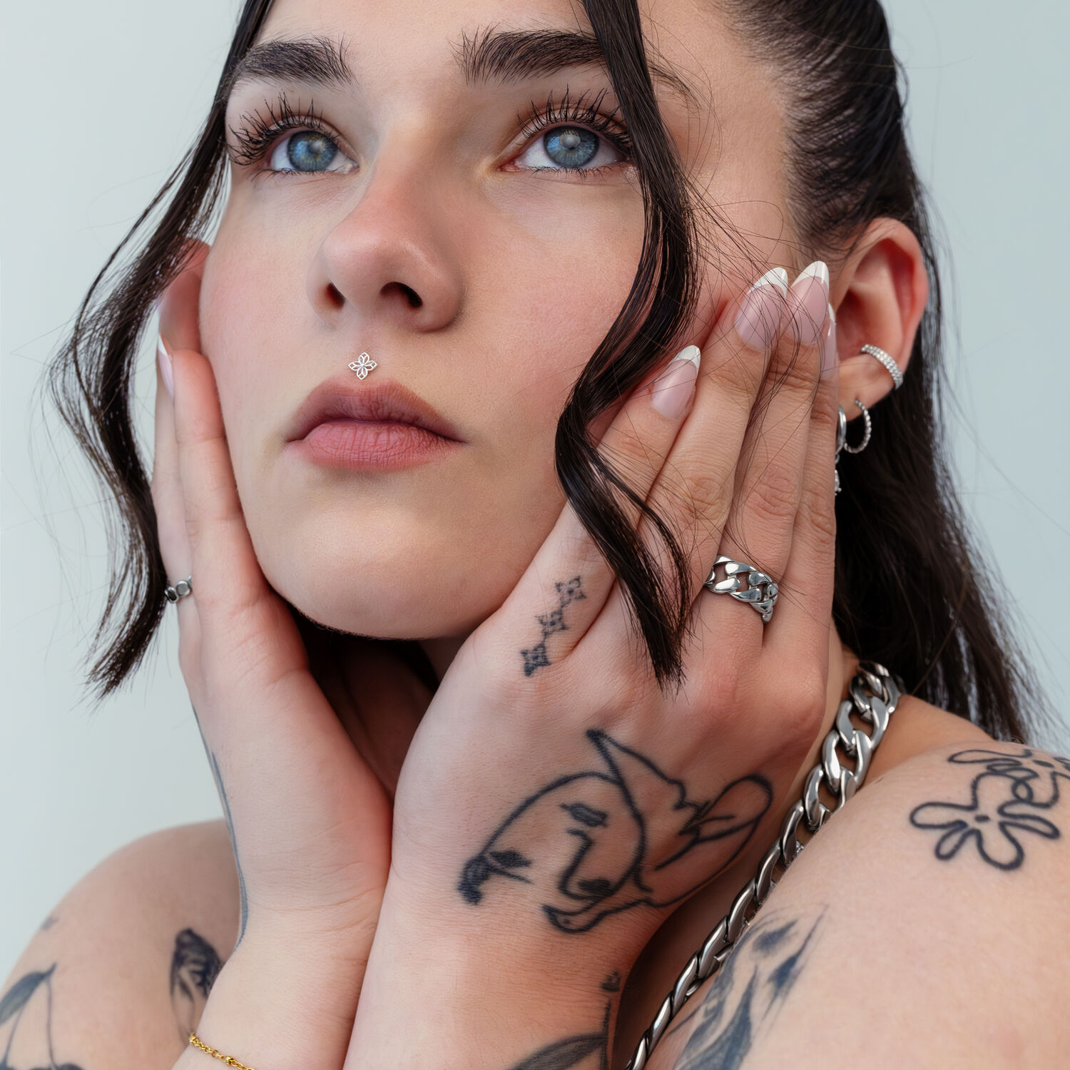 Embout Fleur Argenté Push Fit Femme aux mains tatouées touchant son visage, portant un embout fleur argenté dans le piercing nasal