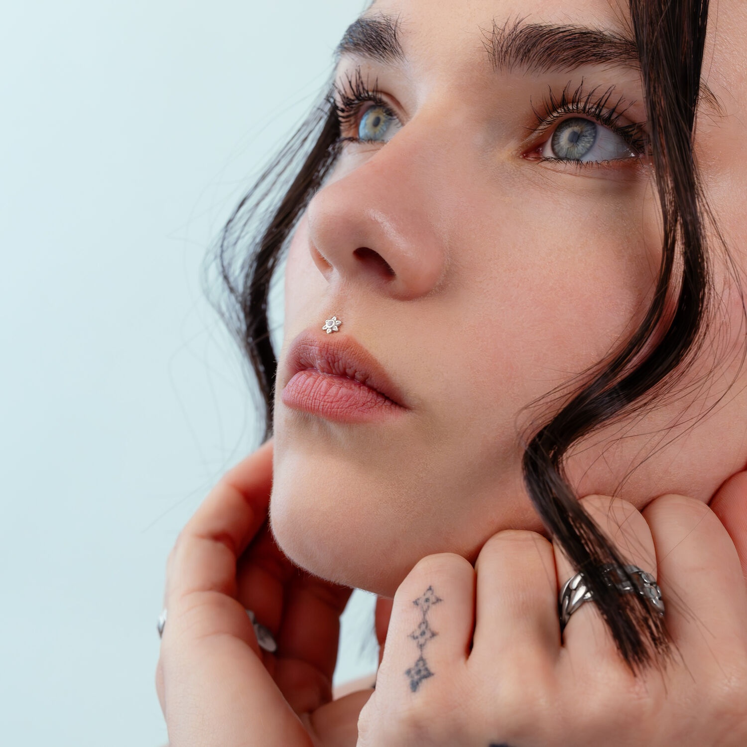Embout Fleur Push Fit en Argent Gros plan d'un visage avec un piercing fleur en argent sur le nez, fond bleu clair