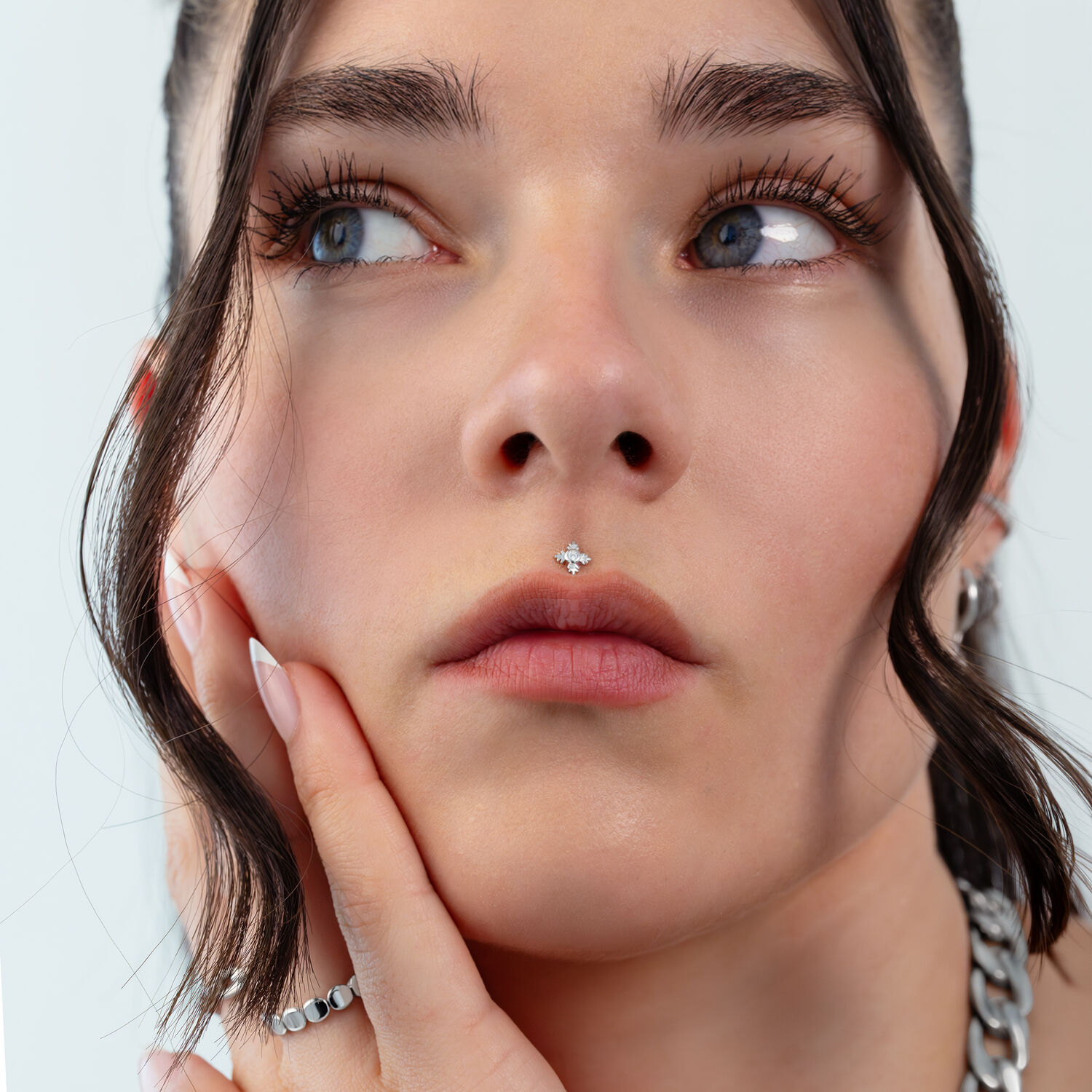 Gros plan d'un visage avec un piercing feuille argentée au nez, cheveux en arrière-plan