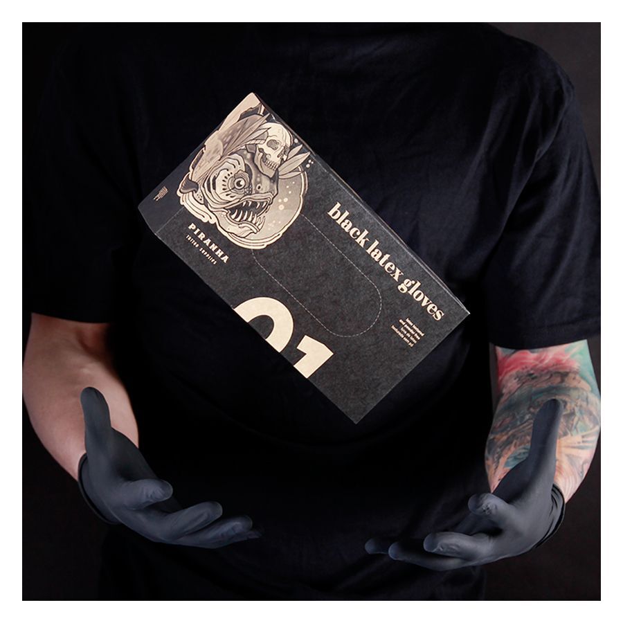 Personne en t-shirt noir tenant une boîte de gants en latex Piranha noirs devant un fond sombre