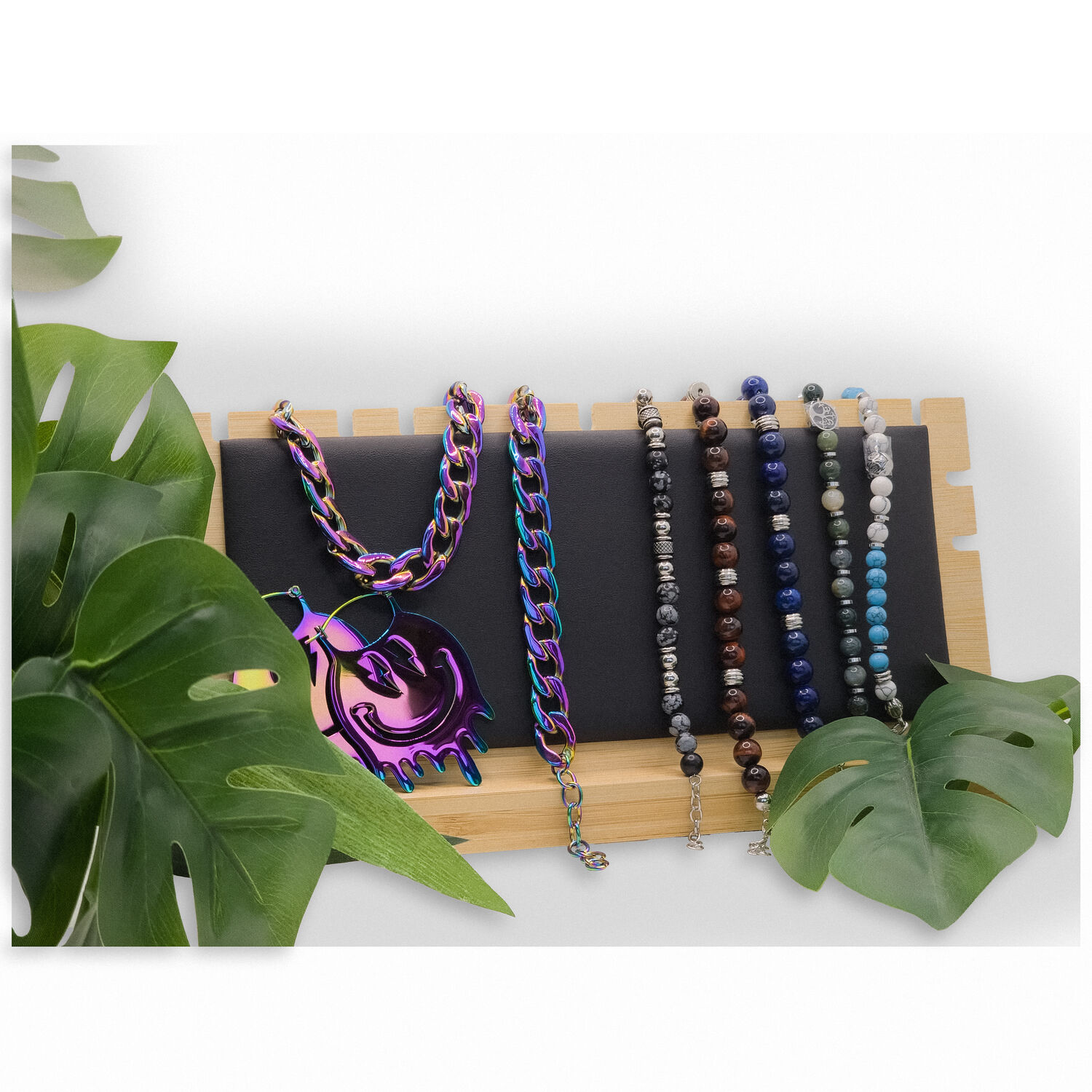 Présentoir à chaînes noir avec bijoux Présentoir en similicuir noir avec des colliers colorés sur bois, entouré de feuilles vertes