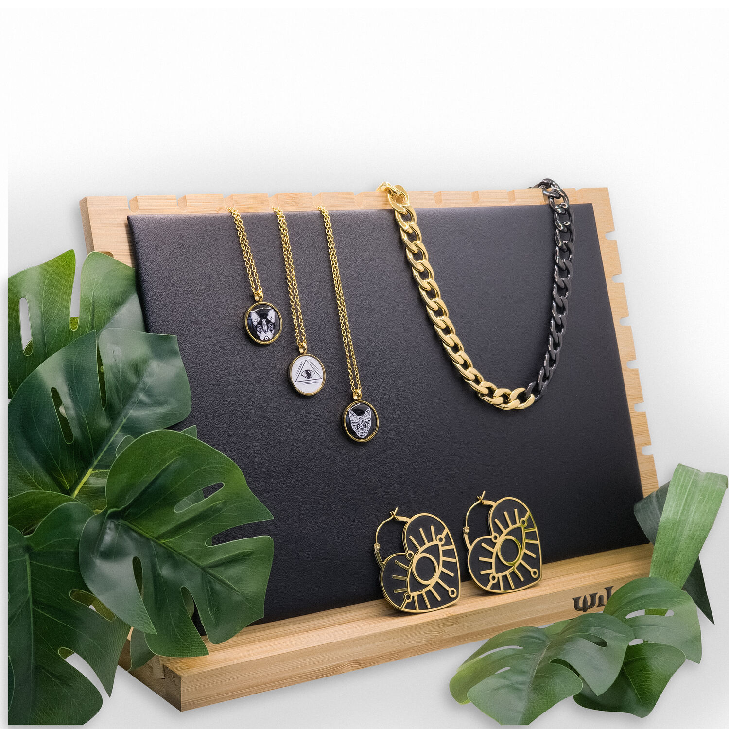 Présentoir à bijoux noir avec chaînes dorées Présentoir à bijoux noir avec chaînes dorées et boucles d'oreilles sur cadre en bois, entouré de feuilles vertes