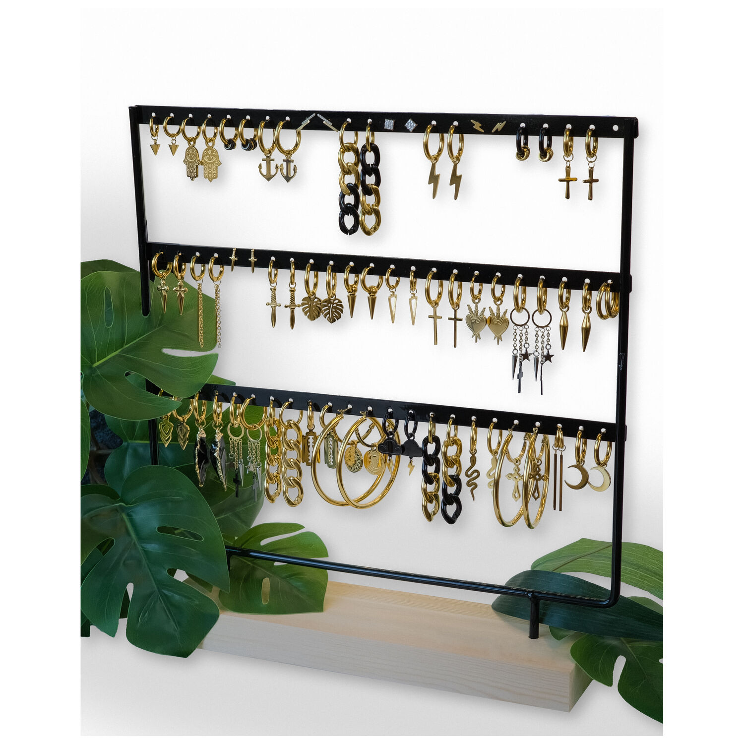 Présentoir noir pour boucles d'oreilles Présentoir en métal noir avec boucles d'oreilles sur base en bois, entouré de feuilles vertes