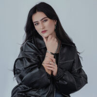 Bague chaîne unisexe en argent et or Femme en blouson en cuir noir portant une bague chaîne en argent et un bracelet assorti sur fond gris